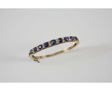 AN EARLY 20TH CENTURY SAPPHIRE AND DIAMOND HALF HINGED BANGLE set to one side with graduated oval-shaped sapphires, each sepa