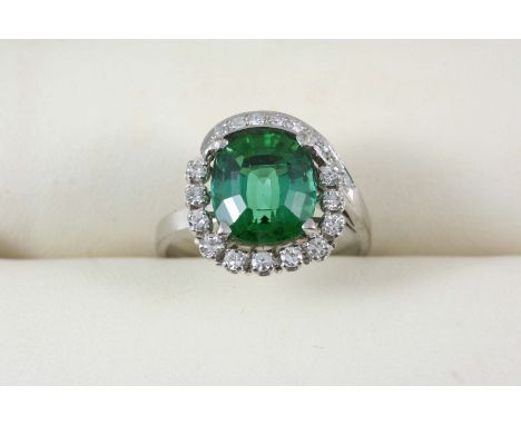 A TOURMALINE AND DIAMOND CLUSTER RING the oval-shaped green tourmaline is set within a surround of circular-cut diamonds, in 