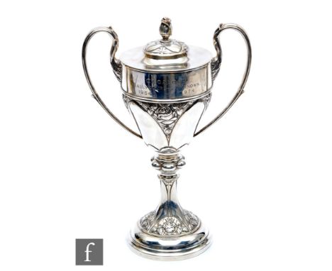 An Arts &amp; Crafts hallmarked silver twin handled trophy cup and cover, part decorated with floral details and terminating 