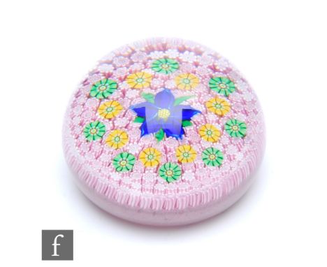A Perthshire glass paperweight, of domed form internally decorated with a central blue stylised lampwork flower, surrounded b