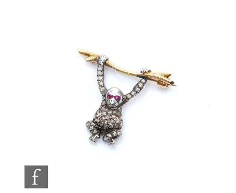 An 20th Century white and yellow gold diamond set brooch modelled as an orangutan with ruby set eyes, hanging from a branch, 