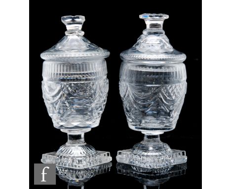A pair of Georgian Irish glass lidded urns, possibly Waterford, circa 1820, the barrel body heavily cut with swags below a bo