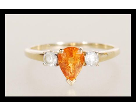 A hallmarked 9ct gold ladies dress ring set with a tear drop cut orange stone flanked by two white accent stones. Hallmarked 