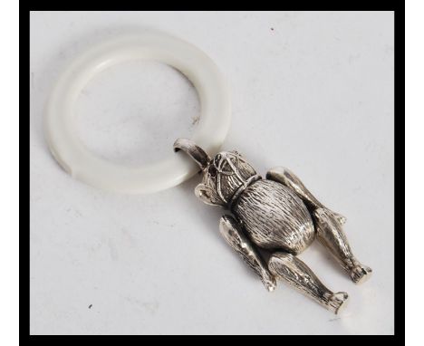 A sterling silver babies teething ring figurine in the form of a bear having articulated legs and arms with ruby eyes. Total 