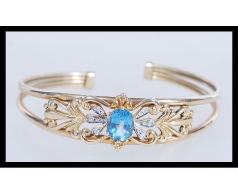 A hallmarked 9ct gold topaz and diamond cuff bangle bracelet having a large central oval mixed cut blue topaz and diamond acc