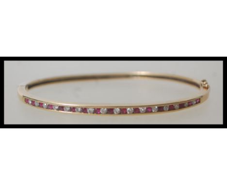 A 9ct 375 stamped bangle bracelet having a pave set alternating line of rubies and diamonds. The bangle of circular form havi