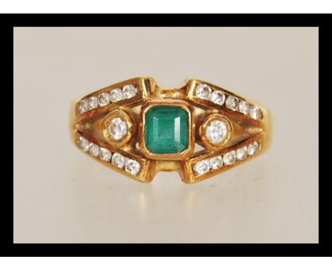 A stamped 750 18ct gold ladies dress ring set with a square cut emerald within a split shank having diamond accent stones. We