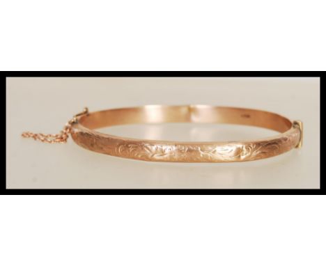 A hallmarked 9ct gold bangle bracelet with engraved floral decoration to front, having hinged opening with tongue and groove 