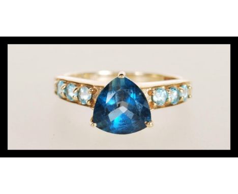 A hallmarked 9ct gold ring set with a triangular cut blue stone with light blue accent stones to the shoulders. Hallmarked Bi