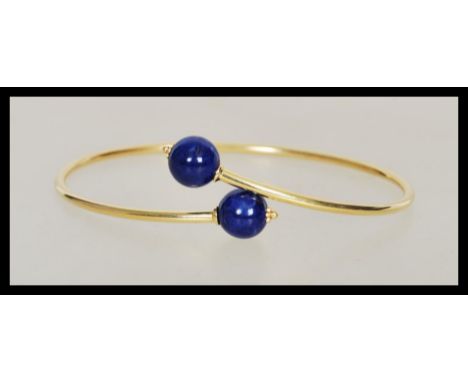 A stamped 750 18ct gold bangle bracelet finished with two blue bead stoppers. Weight 4.3g. Measures 1 1/4 inches at the wides