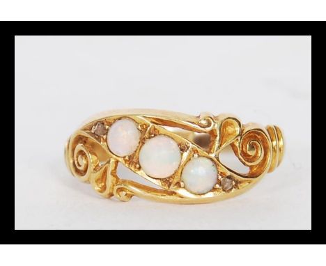 A late 19th Century / early 20th Century 18ct gold ring set with three opal cabochons having scrolled and pierced decoration.