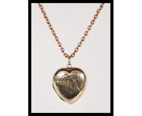 A 20th Century stamped 9ct gold heart locket having scrolled engraving to the front on an unmarked gold tone chain. Total wei