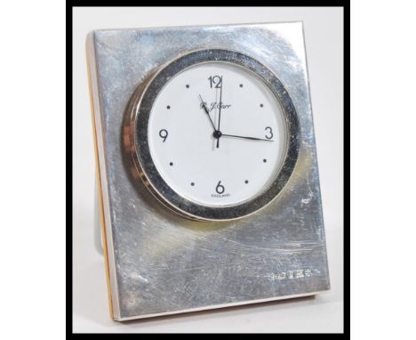 A P. J. Carr silver hallmarked easel back desk clock having a round white enamelled face set within a square silver case on a