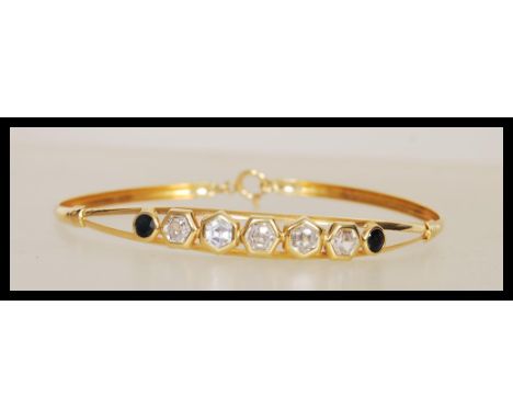 A stamped 750 18ct gold bangle bracelet set with five hexagonal cut white stones and two round cut blue stones, with a lobste