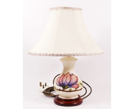 A Moorcroft magnolia pattern table lamp, decorated against an ivory ground, with cream shade. 