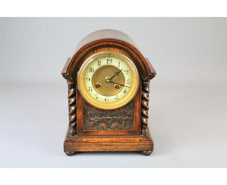 An Edwardian Oak Mantel Clock. The clock with domed case, gilt brass and cream chapter ring with Arabic dial, flanked by two 