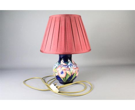 A 20th Century Moorcroft Lamp Base. The lamp base painted with orchid on blue ground, approx 30 cms with burgundy shade.