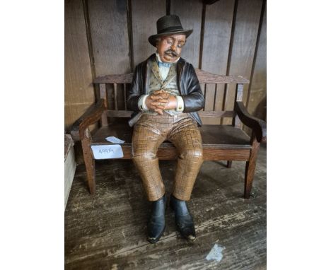 A Bernard Bloch pottery figure of a man seated on a wooden bench.