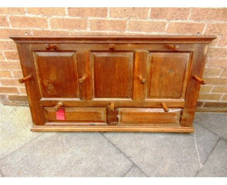 AN OAK COAT RACK,  fitted with ten carved oak pegs to a backboard with five fielded panels, 120cm wide 67cm high