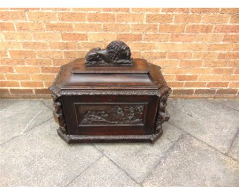 A CARVED OAK CELLARETTE,  the caddy top surmounted by a seated lion, the front decorated with a panel depicting Christ in the