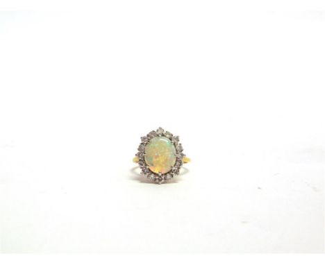 AN OPAL AND DIAMOND CLUSTER RING stamped '18ct', the oval shallow cabochon measuring 11.6mm by 10mm by 2.5mm deep, enclosed b