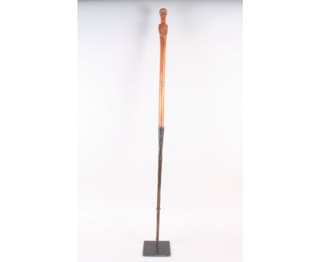 An African/tribal iron mounted spear/stick, the wood handle carved as a female figure, 43" long, with museum style stand