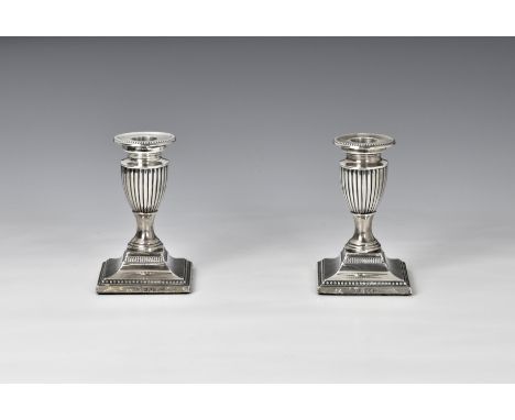 A pair of late Victorian dwarf candlesticks Charles Stuart Harris, London 1898, the stepped square beaded base rising to urn 