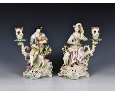 A pair of late 18th century Derby porcelain figural candlesticks the seated figures of a man playing bagpipes with a dog at h