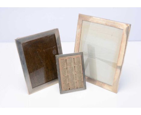 Three Art Deco period silver photograph frames, the largest with engraved initials and 29cm by 23cm, the smallest with perpet