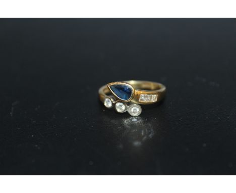 AN UNUSUAL HALLMARKED 18 CARAT GOLD SAPPHIRE AND DIAMOND RING, in a crossover style with a teardrop shaped sapphire estimated