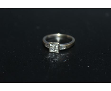 A SIX STONE DIAMOND RING, having four Princess cut diamonds set in a square in a rub over setting with a tapering baguette cu