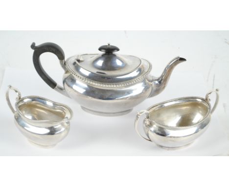 BARKER BROS SILVER LTD; a George V hallmarked silver three piece tea set comprising a squat oval teapot with cast rim, ebonis