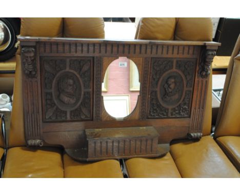 An early 20th century oak hall panel centred with an oval mirror above lidded compartment, flanked by carved busts of gentlem