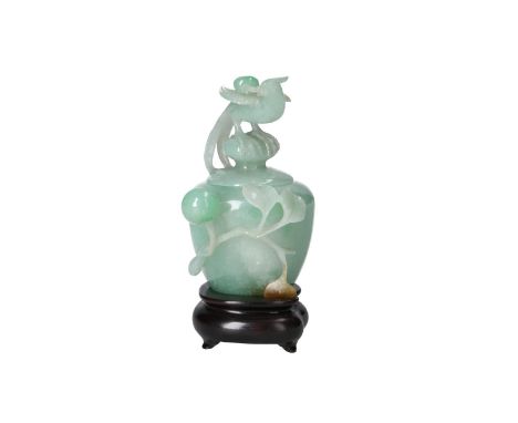 A jade lidded cup, with relief decor of a fruit and leaves, on wooden stand. The knob of the lid in the shape of a bird of pa