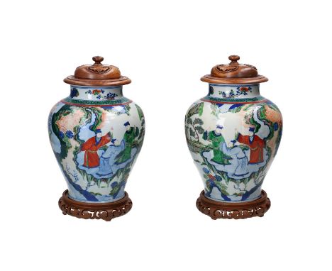 A pair of wucai porcelain vases with carved wooden lids and bases, decorated with figures in a garden. Unmarked. China, 19th/
