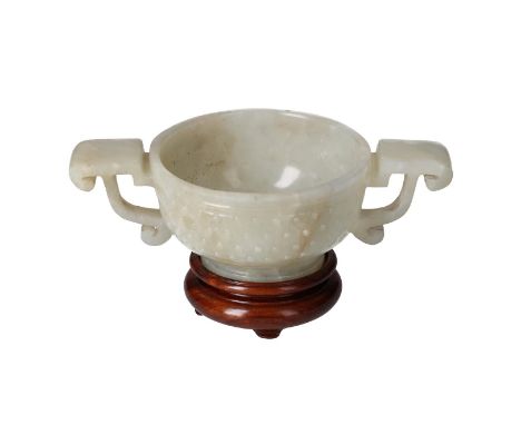 A jade libation cup with two handles and dotted relief decor, on wooden stand. China, 19th century.L. cup 12.5 cm. H. excl. s