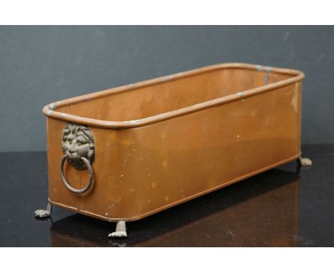 A copper rectangular planter with brass lion head handles. 