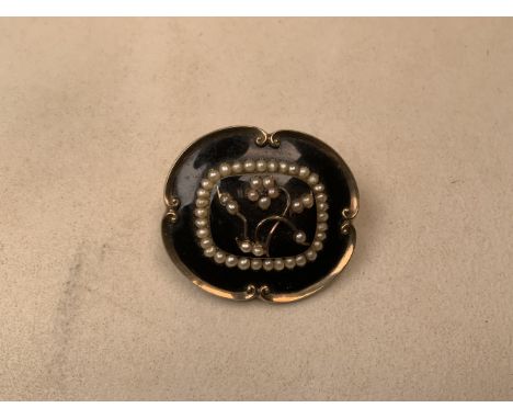 A Victorian black enamel and yellow metal mourning brooch with seed pearl accents and quartz crystal back. 26g. 5cm x 4cm.