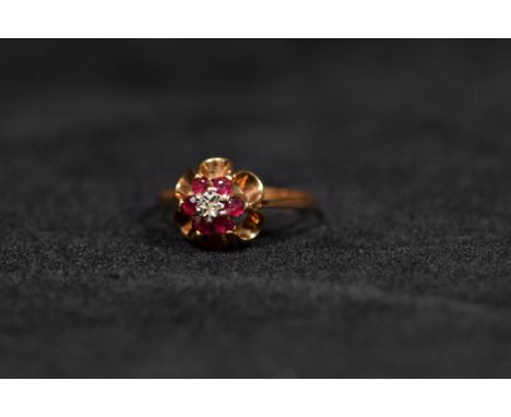 A 9ct gold ruby and diamond ring. Central illusion set diamond with a surround of six round free cut rubies to an open work s