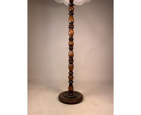 A wooden turned floor lamp with a fringed shade. H:175cm (with shade)