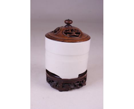 A CHINESE CERAMIC CYLINDRICAL TRIPOD INCENSE BURNER Blanc de Chine, moulded with raised band with carved wooden stand and pie