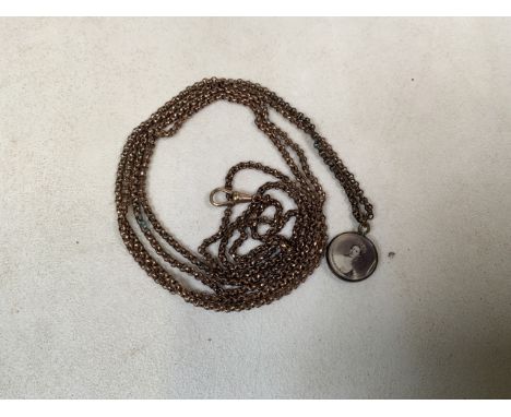 An unmarked yellow metal long guard watch chain with lobster clasp and commemorative locket with portrait of young and older 