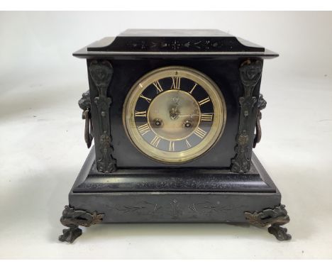 A French black slate mantle clock with bronzed metal feet and lion loop carrying handles. Gilt brass face with black chapter 