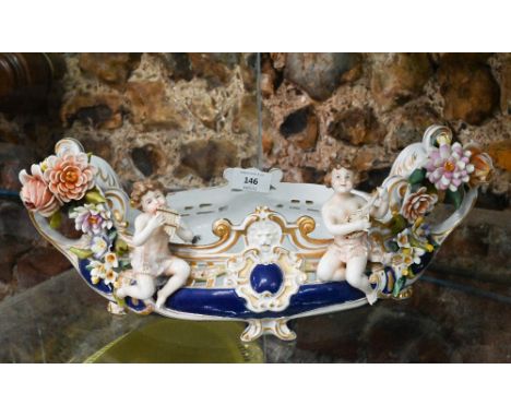 A Continental porcelain oval flower trough mounted with two musical putti and encrusted with flowers, 40 cm wide