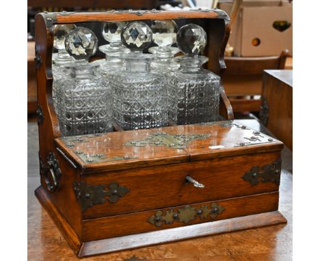 A late Victorian oak brass mounted tantalus compendium housing three cut glass decanters, twin-hinged games box over secret d