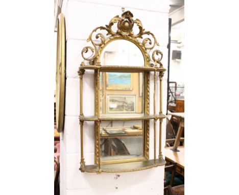 A decorative gilt framed mirror with open work cresting and three shelves.
