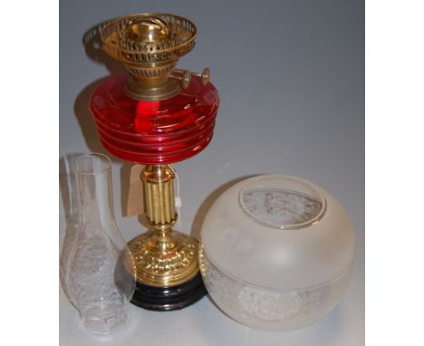 An early 20th century oil lamp having an etched opalescent globular shade over a red tinted glass font to a fluted brass pede