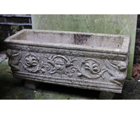 A composite oblong garden plant trough with mask and scrolling foliate decorated frieze, raised on two supports 72cm