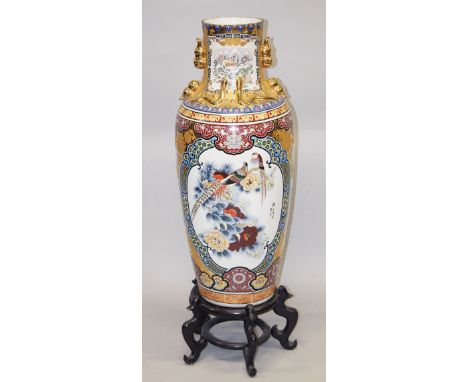 A LARGE CHINESE FLOOR STANDING PORCELAIN VASE on a hardwood stand, decorated in Japanese style with a large panel of a peacoc