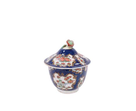 A Worcester sucrier and cover, circa 1770, decorated in the Kakiemon style with foliate panels on a blue scale ground, pseudo